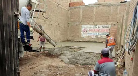 Obreros vacían concreto con una canaleta en un terreno entre muros