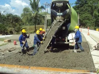 Obreros esparciendo con lampas el concreto que sale de un mixer sobre una pista